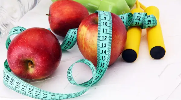 Jabłka, miarka i sprzęt do ćwiczeń symbolizują zdrowe nawyki. Pytasz jakie owoce na odchudzanie? Jabłka to świetny wybór!