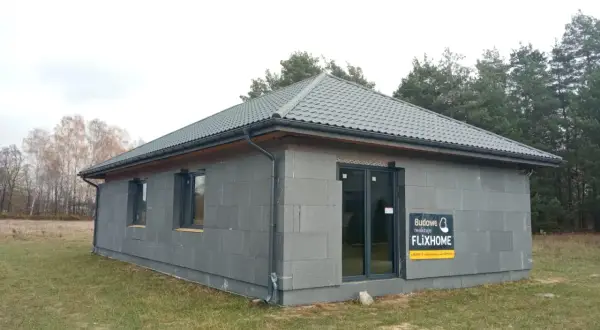 Gotowe domy pod klucz do 150 tys. zł. Nowoczesny, parterowy budynek z szarej cegły, z szarym dachem i dużymi oknami.