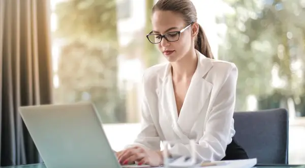 Kobieta w okularach pracuje na laptopie, planując swoją działalność nierejestrowaną.