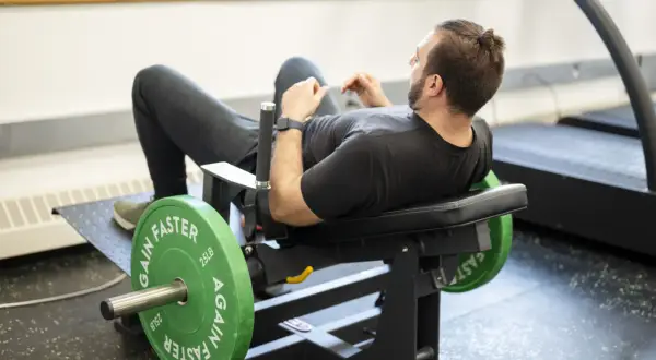 Man tränar höfterna på en hip thrust maskin med viktskivor.