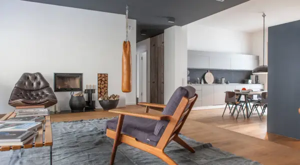 Ein Wohnzimmer mit Kamin, Ledersessel und einem Holzstuhl. Die Kombination von Holzarten im Boden und Möbeln schafft eine warme Atmosphäre.