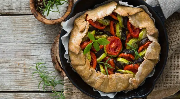 Tarte aux légumes colorée, garnie de tomates, courgettes et aubergines, prête à être dégustée.