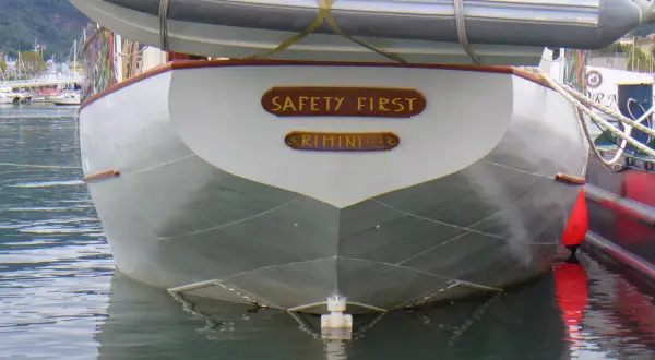 La poppa di una barca con la scritta "SAFETY FIRST RIMINI". Il suo mascone, simbolo di sicurezza, è ben visibile.