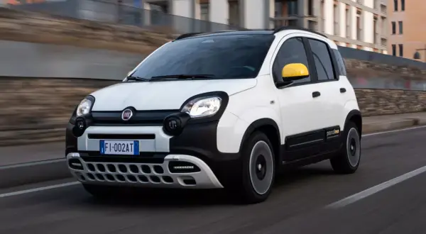 Biały Fiat Pandina z żółtymi lusterkami pędzi po drodze.