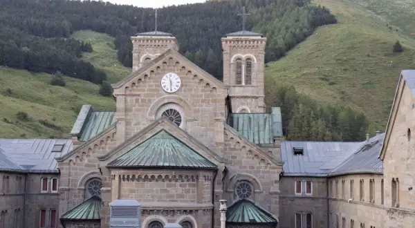 Bazylika Matki Bożej z La Salette, kamienna budowla z wieżami i zegarem, wznosi się na tle zielonych górskich zboczy.
