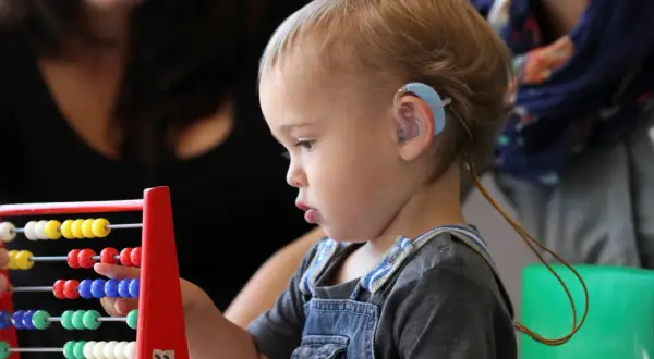 Niño con audífono jugando con ábaco, explorando la caja de los sentidos oido.