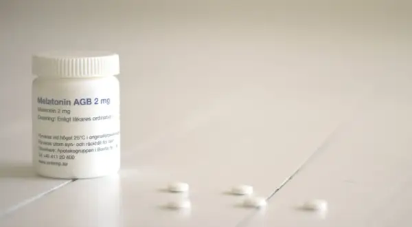 En burk med melatonin till barn, 2 mg, står på ett vitt bord. Några tabletter ligger utspridda framför.