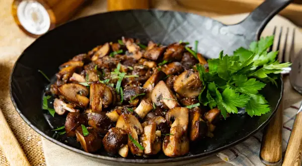 Gebratene Champignons in einer Pfanne, garniert mit frischer Petersilie. Ein köstliches Gericht, das zum Genießen einlädt.