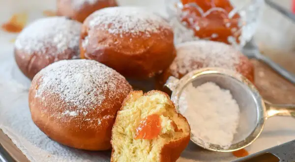 Rosquillas de naranja recién hechas, espolvoreadas con azúcar glas. Una está partida, mostrando su relleno de mermelada.