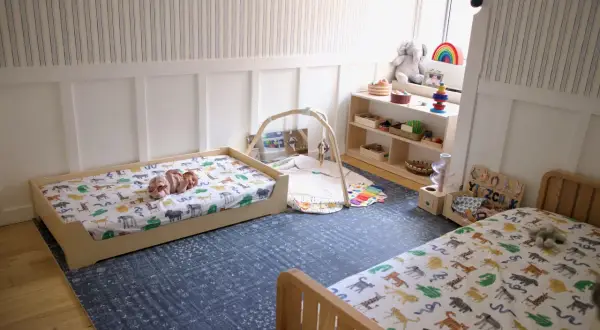 A baby sleeps on a floor bed with animal print sheets, showcasing floor bed safety in a nursery.