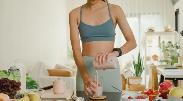 Frau mixt einen Smoothie, der zeigt, wie Proteinpulver beim Abnehmen helfen kann. Gesunde Zutaten liegen bereit.