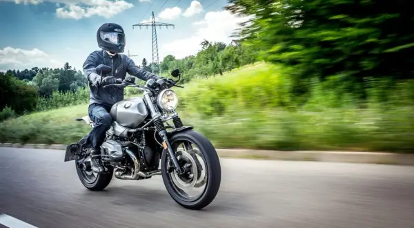 Motocyklista w kasku i kurtce jedzie drogą. Kask i kurtka to obowiązkowe wyposażenie motocykla, zapewniające bezpieczeństwo.