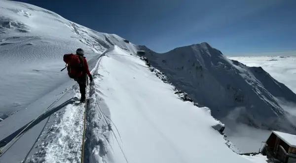 Bergsteiger auf dem Weg zum Mont Blanc besteigen, gesichert durch ein Seil, mit atemberaubendem Blick auf schneebedeckte Gipfel und Wolkenmeer.