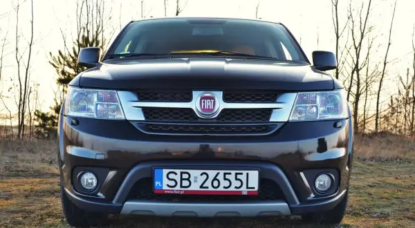 Czarny Fiat Freemont na tle drzew. Zastanawiasz się nad jego spalaniem? Ten SUV oferuje przestronne wnętrze i komfort podróżowania.