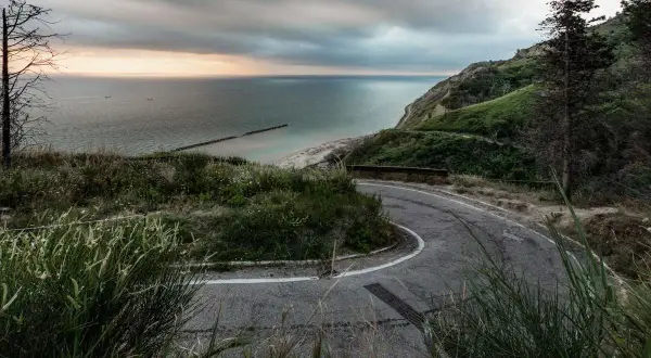 Strada tortuosa nel parco naturale regionale del Monte San Bartolo, con vista sul mare Adriatico e una spiaggia sabbiosa.