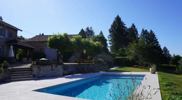 Belle propriété avec piscine, un projet de création bassin réussi. La maison en pierre et les arbres créent un cadre idyllique.