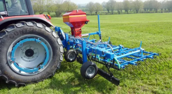 Tracteur rouge avec semoir bleu pour le sursemis de prairie. L'outil prépare le sol avant de semer de nouvelles herbes.