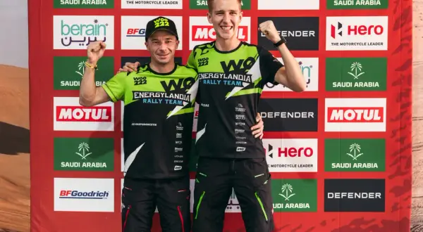 Dwóch zawodników Energylandia Rally Team pozuje z podniesionymi pięściami na tle baneru z logo sponsorów.