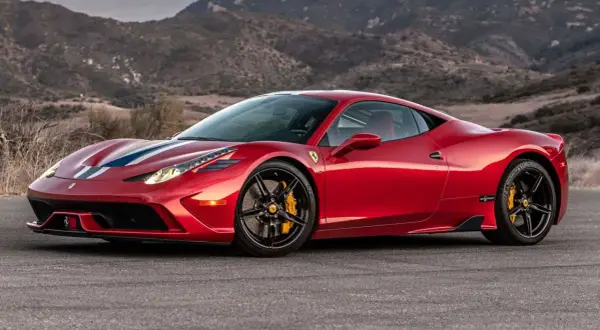 Czerwone Ferrari 458 z białymi i niebieskimi pasami na masce, zaparkowane na tle górskiego krajobrazu.