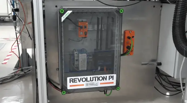 Wewnątrz przezroczystej obudowy widać system sterowania z napisem "REVOLUTION PI POWERED BY Raspberry Pi". To pokazuje, że raspberry co to za urządzenie, które zasila ten przemysłowy komputer.
