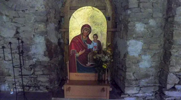 Ikona Matki Boskiej z Dzieciątkiem w kamiennej niszy cerkwi w Łopience. Obok świecznik.