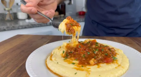 Un tenedor levanta una porción de polenta con tuco, mostrando su textura cremosa y la rica salsa de carne y tomate.
