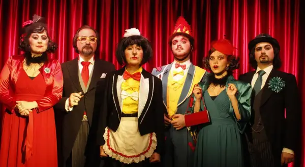 Sei personaggi in costume, forse per la cantatrice calva trama, posano davanti a una tenda rossa.