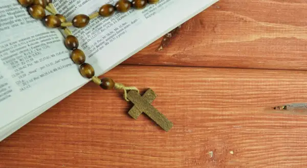 Różaniec na drewnianym stole obok Biblii, przypominający o 5 przykazaniach kościelnych.