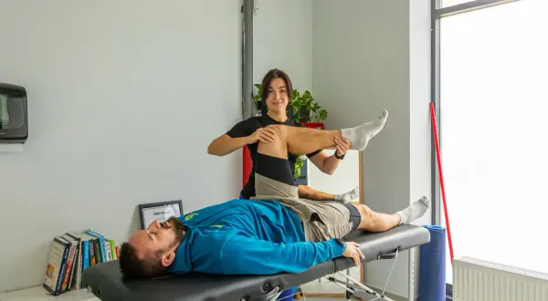 Fizjoterapeuta wykonuje ćwiczenie z pacjentem leżącym na kozetce.