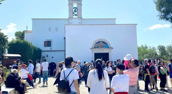 Folla di fedeli davanti alla chiesa di Santa Maria di Merino, con il campanile e un mosaico sopra l'ingresso.