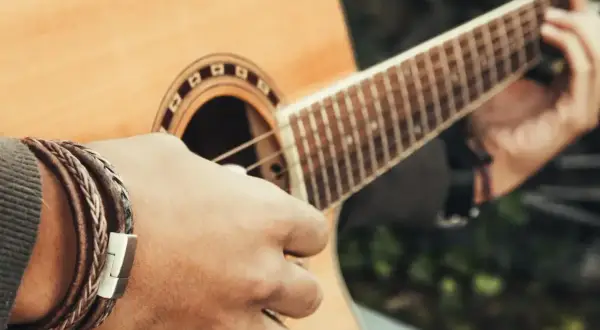 Dłoń z bransoletką gra na gitarze, tworząc dźwięki w tonacji c-dur.