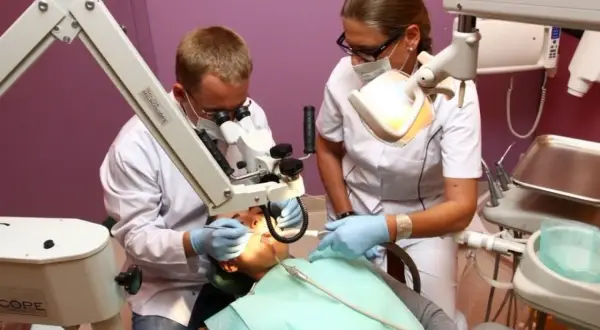 Dentysta i asystentka pracują przy pacjencie pod mikroskopem w gabinecie stomatologicznym.