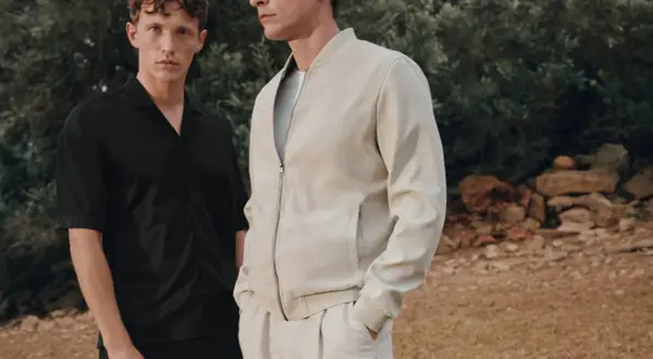 Zwei Männer im lässigen Party-Chic-Look: Einer trägt ein schwarzes Hemd, der andere eine cremefarbene Bomberjacke.