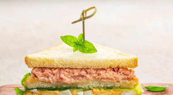 Tramezzini veloci con tonno, uova e lattuga, guarniti con basilico fresco. Perfetti per un pasto rapido e gustoso.