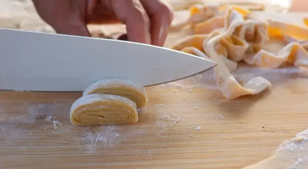 Eine Hand schneidet mit einem Messer frisch gemachte Nudeln. Das ist der Beginn von hausgemachten Nudeln.