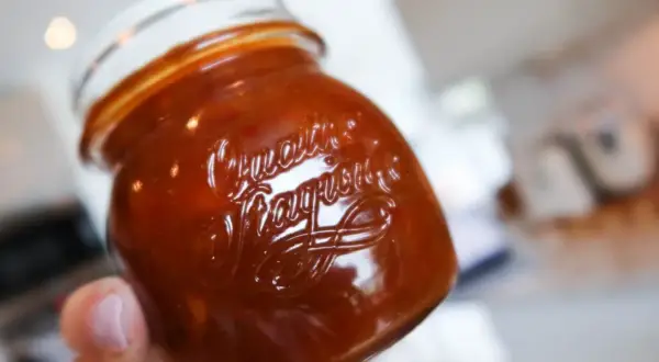 En hand håller ett glas med en mörkröd rabarber chutney. Texten "Quartier" och "Fragrance" syns i glaset.