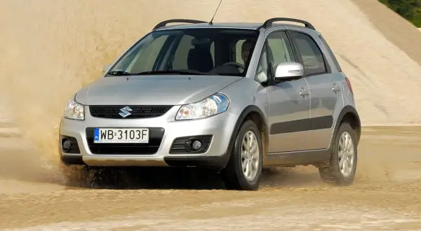 Srebrny Suzuki SX4 1.6 benzyna pokonuje piaszczystą wydmę, wzbijając tumany kurzu.