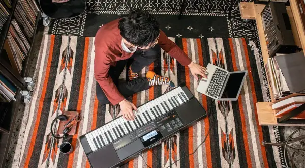 Mężczyzna gra na keyboardzie Casio, obok laptop i słuchawki.