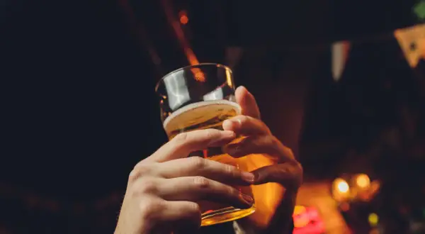 Dwie dłonie trzymające szklankę piwa, w tle rozmyte światła i chorągiewki. Czy piwo tuczy?