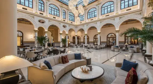 Elegante lobby del spa hotel Miramar, con sofás curvos, mesas y grandes lámparas de araña bajo un techo de cristal.