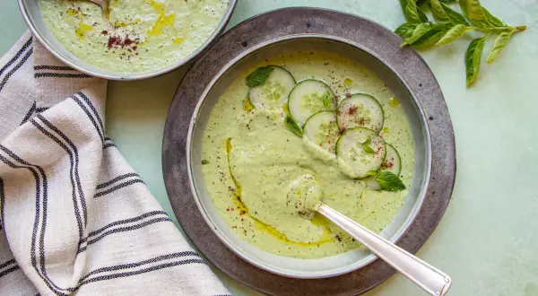 Deux bols de soupe froide aux concombres et menthe, arrosés d'huile d'olive et saupoudrés d'épices.