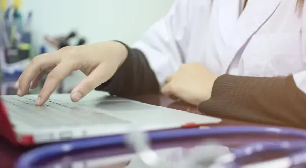 Lekarz wpisuje dane pacjenta na laptopie, co oznacza skierowanie na cito. Stetoskop leży obok.