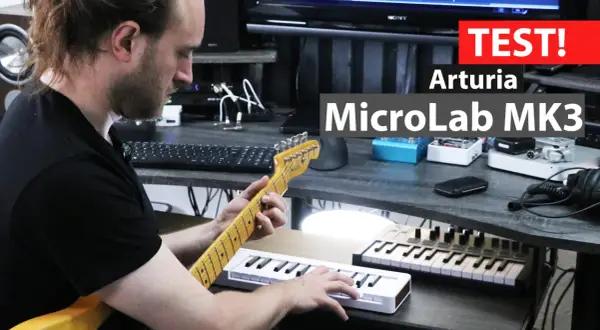 Mężczyzna gra na gitarze, obok niego leży biały midi keyboard Arturia MicroLab MK3.