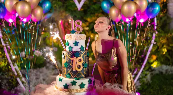 Dziewczyna zdmuchuje świeczki z tortu na 18. urodziny, otoczona balonami i fajerwerkami. To z pewnością jedne z tych szalonych pomysłów na 18 urodziny, które zapadają w pamięć!