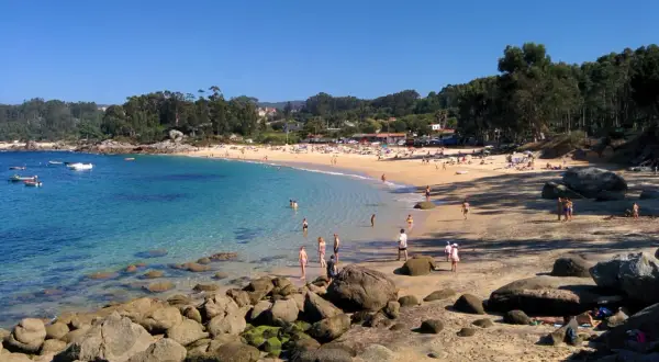 Gente disfrutando del sol y el mar en la Praia da Mourisca, con aguas cristalinas y arena dorada.