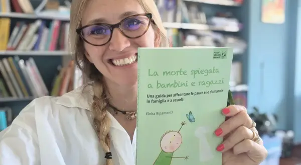 Donna sorridente con libro "La morte spiegata a bambini e ragazzi", affronta la paura di morire e lasciare i figli.