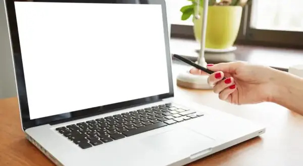 Dłoń z czerwonymi paznokciami wskazuje na biały ekran laptopa.