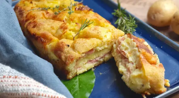 Polpettone di patate dorato e invitante, con strati di prosciutto e formaggio, guarnito con rosmarino e timo.