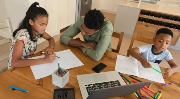 Familie lernt zu Hause. Ist Homeschooling in Deutschland erlaubt? Kinder schreiben und malen, Vater hilft.