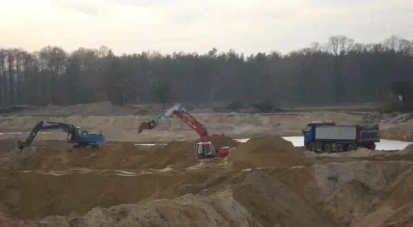 Koparki i wywrotka pracują na placu budowy, wykonując prace ziemne.
